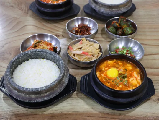 돌솥밥과 날계란을 넣은 순두부찌개, 반찬 다섯 가지 — 뒤로 뚝배기와 돌솥이 하나씩 더